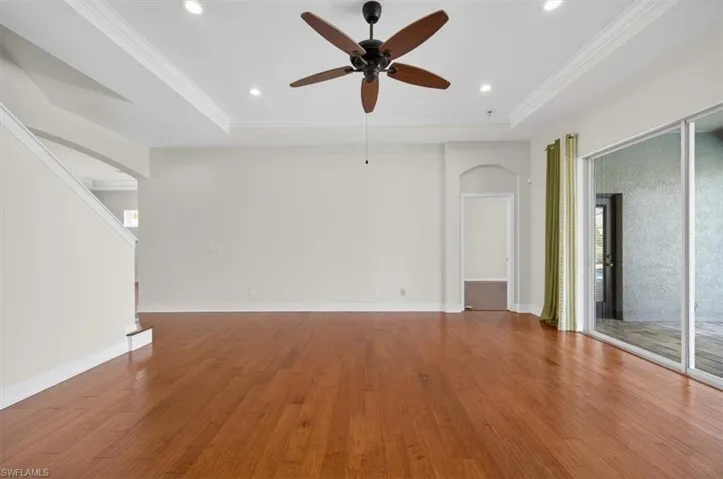 Unfurnished living room featuring arched walkways, a ceiling fan, wood finished floors, a tray ceiling, and recessed lighting