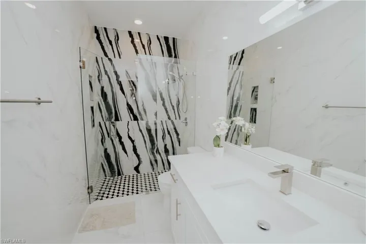 Bathroom featuring vanity, toilet, a tile shower, and tile walls