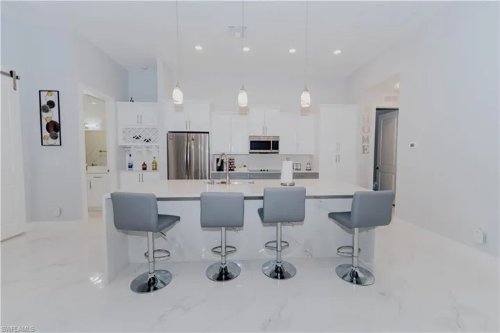 Kitchen featuring decorative light fixtures, sink, appliances with stainless steel finishes, a center island with sink, and white cabinets