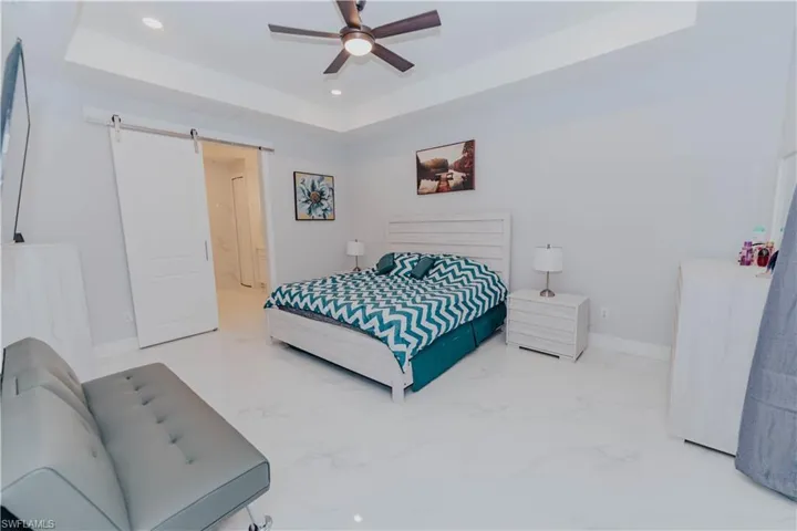 Bedroom featuring a barn door, a tray ceiling, and ceiling fan