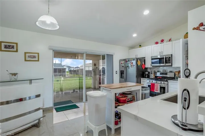 Kitchen with tasteful backsplash, stainless steel appliances, vaulted ceiling, decorative light fixtures, and white cabinets