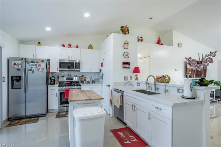 Kitchen with lofted ceiling, stainless steel appliances, a peninsula, light stone countertops, and white cabinetry