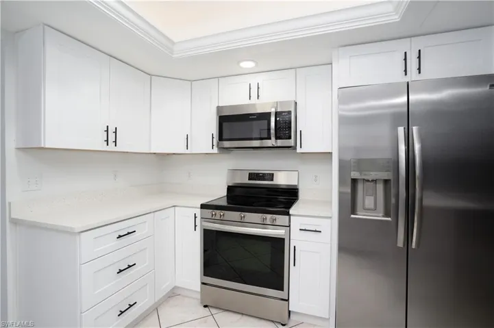 Kitchen with a raised ceiling, stainless steel appliances, light tile patterned floors, and white cabinetry