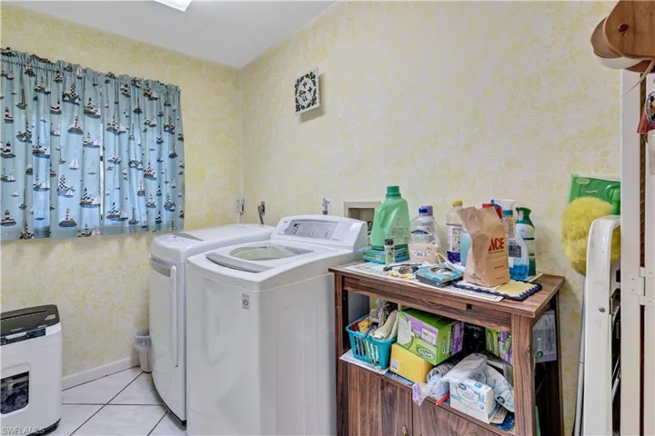 Clothes washing area with light tile patterned floors and washing machine and dryer