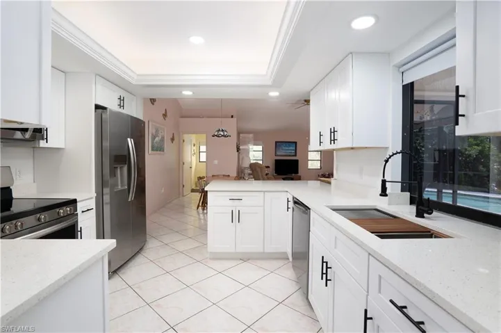 Kitchen with appliances with stainless steel finishes, light stone countertops, white cabinetry, and sink