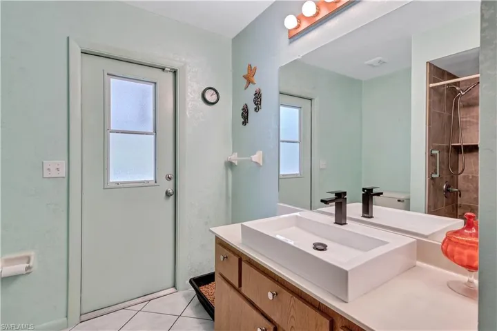 Bathroom with tile patterned flooring, a wealth of natural light, a tile shower, and vanity