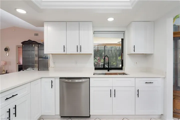 Kitchen featuring light stone counters, sink, lofted ceiling, stainless steel dishwasher, and white cabinets