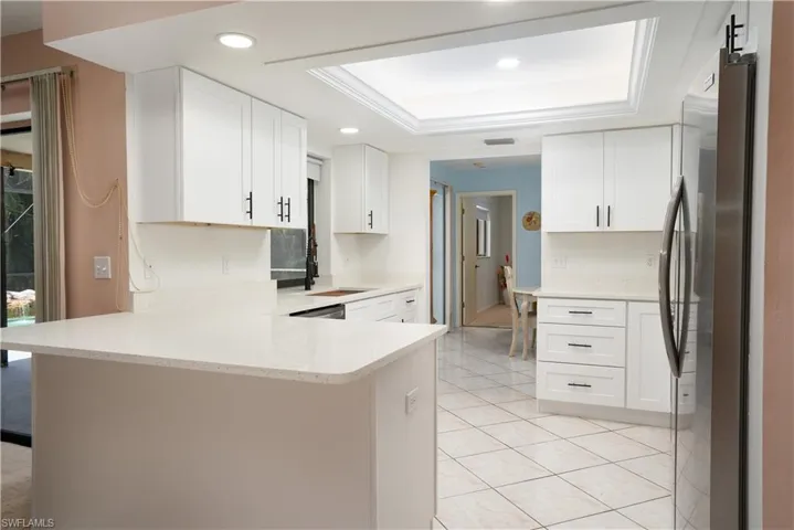 Kitchen featuring a raised ceiling, white cabinetry, kitchen peninsula, and stainless steel refrigerator