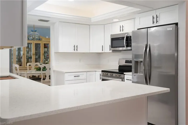 Kitchen featuring white cabinets, appliances with stainless steel finishes, light stone countertops, and a raised ceiling