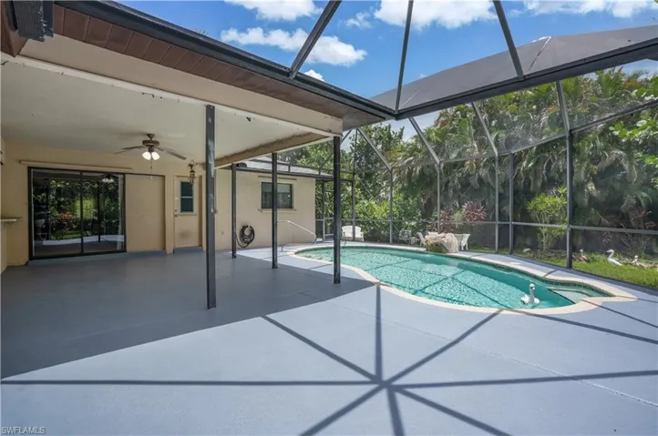 View of pool with glass enclosure, ceiling fan, and a patio area