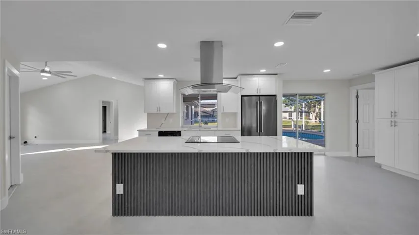Kitchen featuring light stone counters, island range hood, high quality fridge, white cabinetry, and recessed lighting