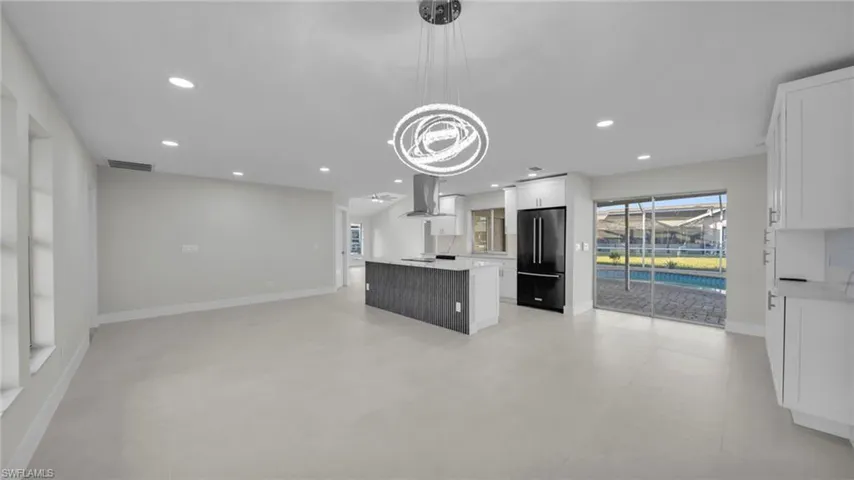 Kitchen featuring white cabinetry, open floor plan, a kitchen island, high end black refrigerator, and range hood