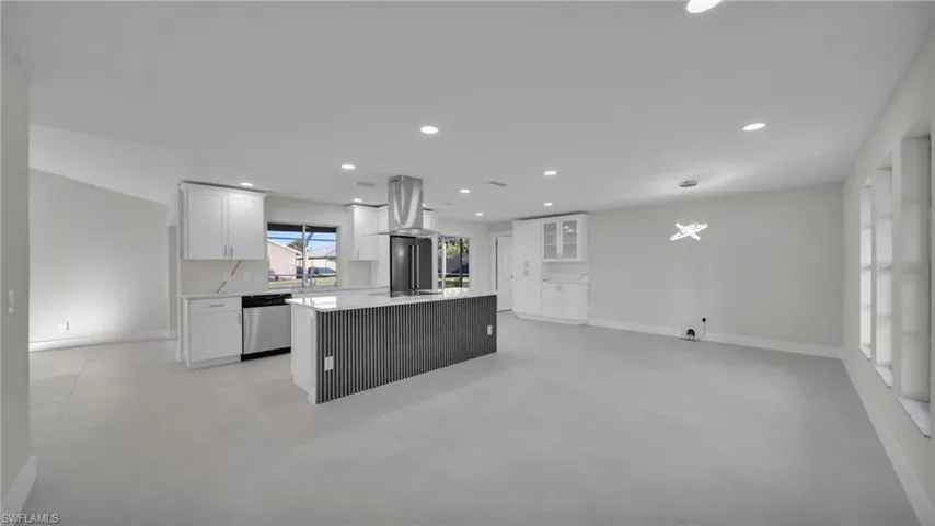Kitchen featuring white cabinetry, a kitchen island, dishwasher, light stone countertops, and open floor plan