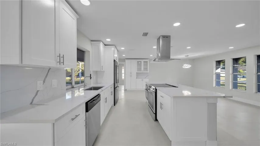 Kitchen with stainless steel appliances, island range hood, glass insert cabinets, and white cabinets