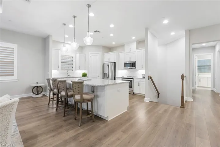 Kitchen with hanging light fixtures, light hardwood / wood-style floors, white cabinets, a kitchen island, and stainless steel appliances
