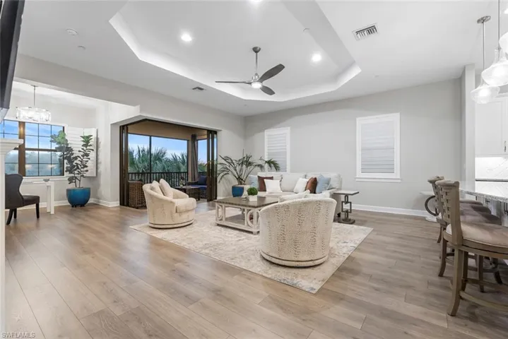Living room with ceiling fan with notable chandelier, hardwood / wood-style flooring, and a tray ceiling