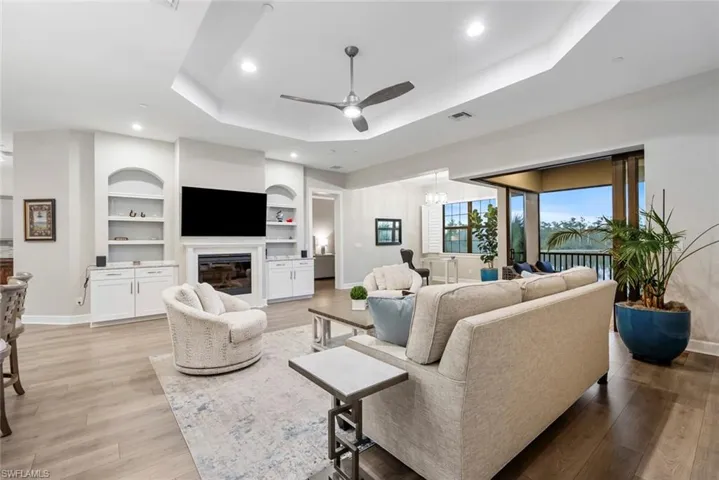 Living room featuring ceiling fan with notable chandelier, built in shelves, a tray ceiling, and light hardwood / wood-style floors