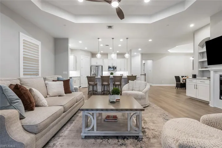 Living room with light hardwood / wood-style floors, a raised ceiling, a fireplace, and ceiling fan