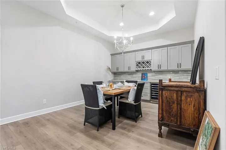 Dining area featuring beverage cooler, light hardwood / wood-style flooring, a chandelier, and a tray ceiling