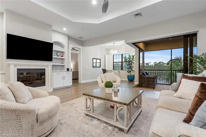 Living room with light wood-type flooring, a raised ceiling, built in features, and a notable chandelier