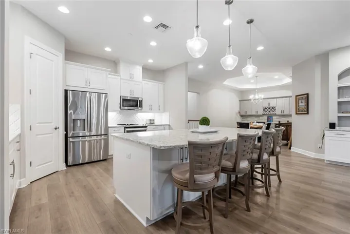Kitchen featuring hanging light fixtures, a kitchen island, white cabinetry, appliances with stainless steel finishes, and light hardwood / wood-style floors