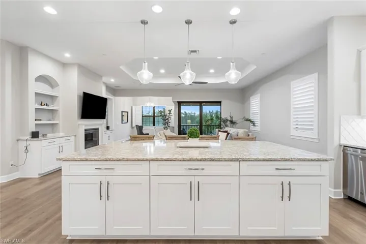 Kitchen with light wood-type flooring, hanging light fixtures, light stone countertops, and white cabinets