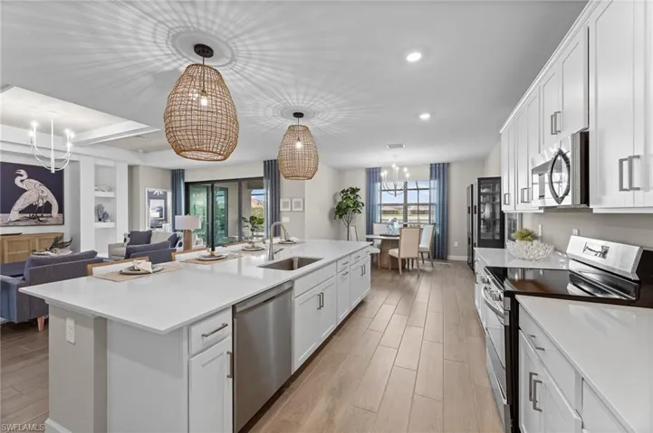 Kitchen with stainless steel appliances, white cabinets, hanging lights, light wood finished floors, and a kitchen island with sink