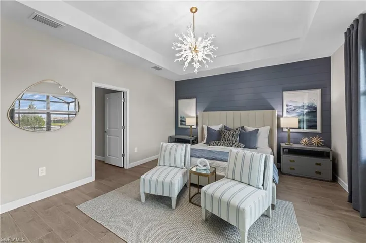 Bedroom with an accent wall, wooden walls, light wood finished floors, a chandelier, and a tray ceiling