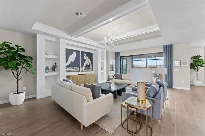 Living area featuring built in features, light wood-style floors, suspended lighting, beamed ceiling, and a raised ceiling