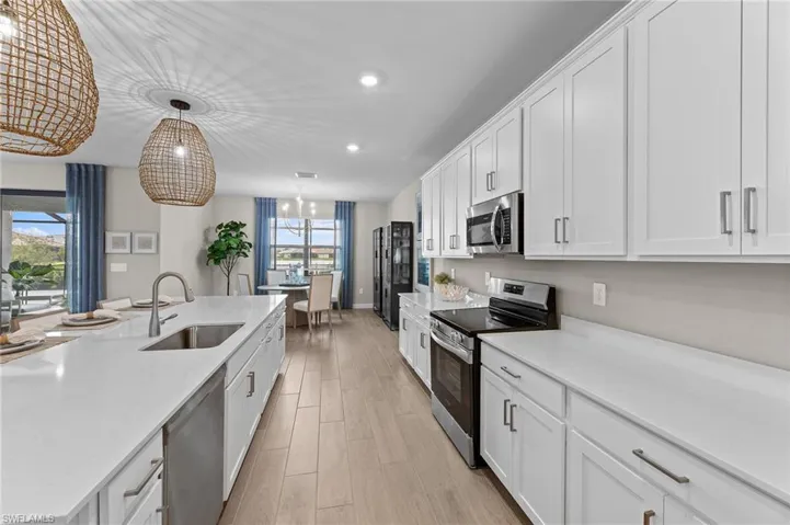 Kitchen featuring stainless steel appliances, white cabinetry, light wood-style floors, light stone counters, and decorative light fixtures