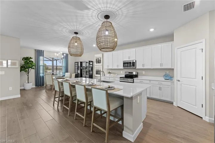 Kitchen with a kitchen breakfast bar, stainless steel appliances, white cabinetry, light wood-style flooring, and a center island with sink
