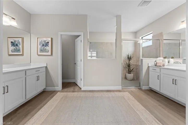 Bathroom featuring two vanities, a stall shower, and light wood finished floors