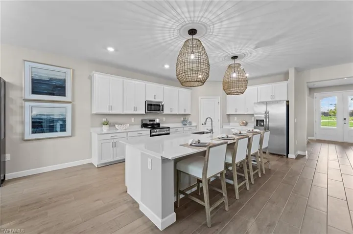 Kitchen featuring wood finish floors, stainless steel appliances, a breakfast bar, white cabinets, and a center island with sink