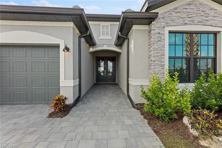 Doorway to property featuring stone siding, stucco siding, french doors, a garage, and driveway