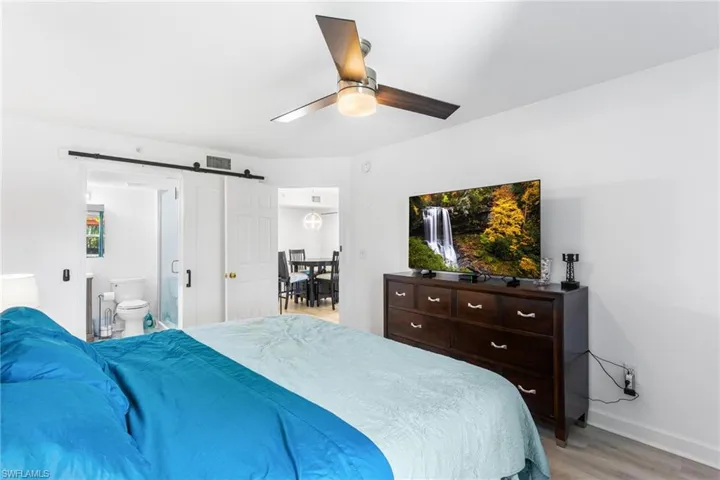Bedroom featuring a barn door, ceiling fan, ensuite bathroom, and light wood-style flooring