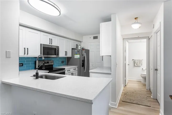 Kitchen with white cabinets, stainless steel appliances, tasteful backsplash, a peninsula, and light wood-style floors