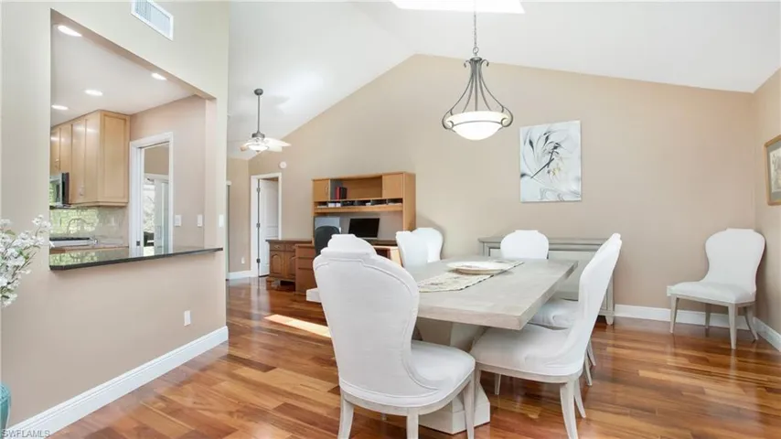 Dining area with high vaulted ceiling, 5" baseboards, wood floors and contemporary clock on the wall.