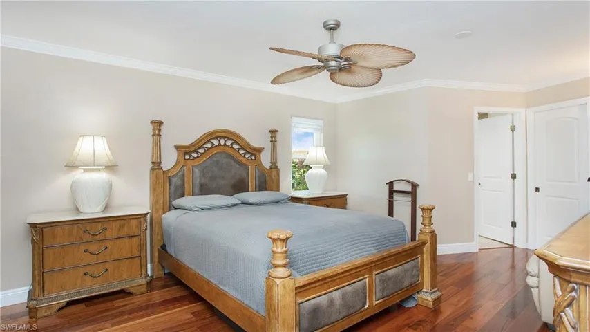 Primary Bedroom with side window, crown molding, 5" baseboards, ceiling fan, and wood flooring