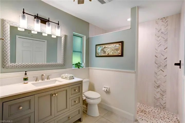 Bathroom with a tile shower, tile flooring, vanity, and toilet