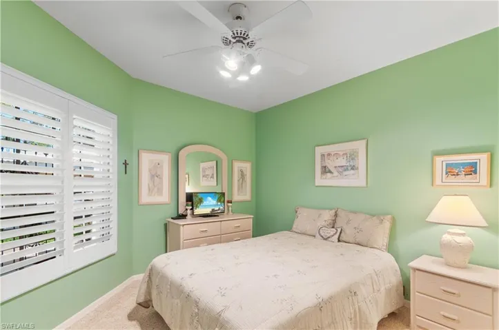 Carpeted bedroom featuring professionally installed Plantation shutters and ceiling fan.