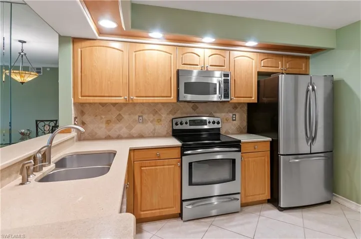 Kitchen featuring decorative backsplash, stainless steel appliances, light countertops, and a sink