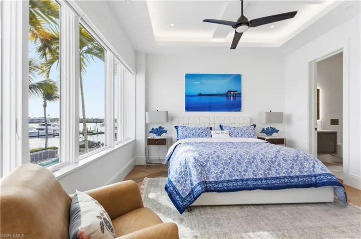 Bedroom with a raised ceiling, a ceiling fan, wood finished floors, and a water view