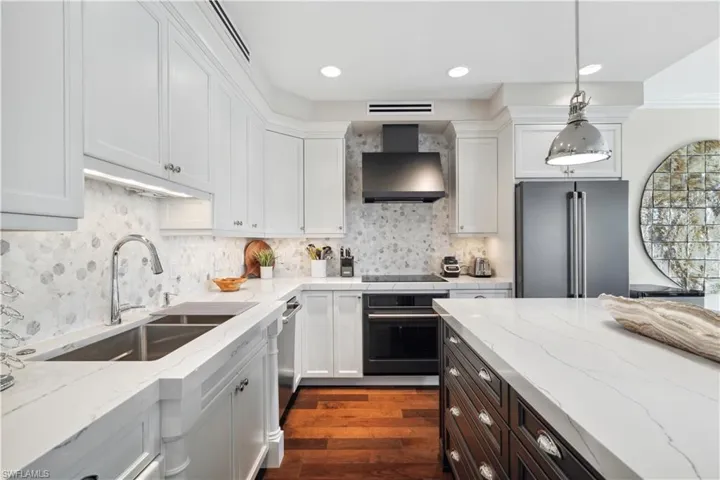 Kitchen with black appliances, tasteful backsplash, wall chimney exhaust hood, sink, and dark wood-type flooring