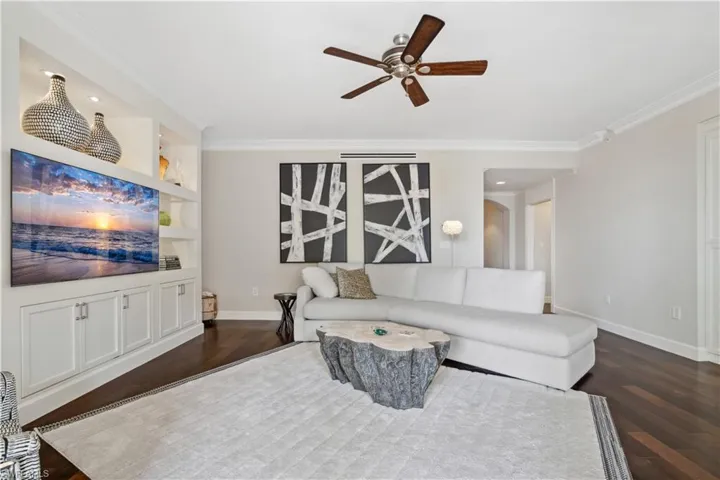 Living room with ornamental molding, dark hardwood / wood-style flooring, built in shelves, and ceiling fan