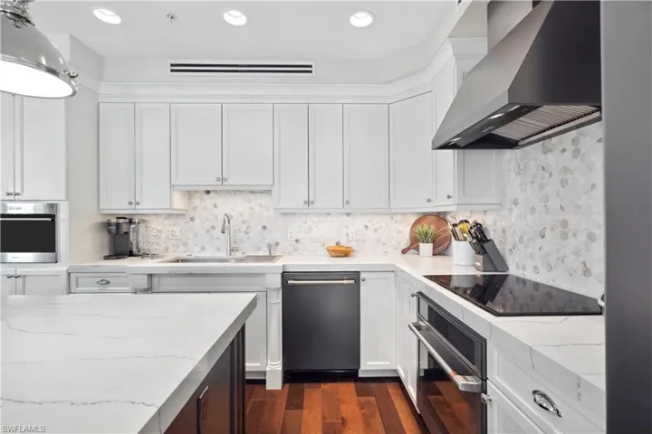 Kitchen featuring dark wood-type flooring, wall chimney exhaust hood, appliances with stainless steel finishes, decorative backsplash, and sink