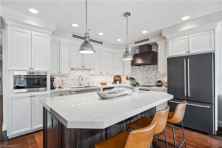 Kitchen with stainless steel oven, wall chimney range hood, a center island, dark wood-type flooring, and high end refrigerator