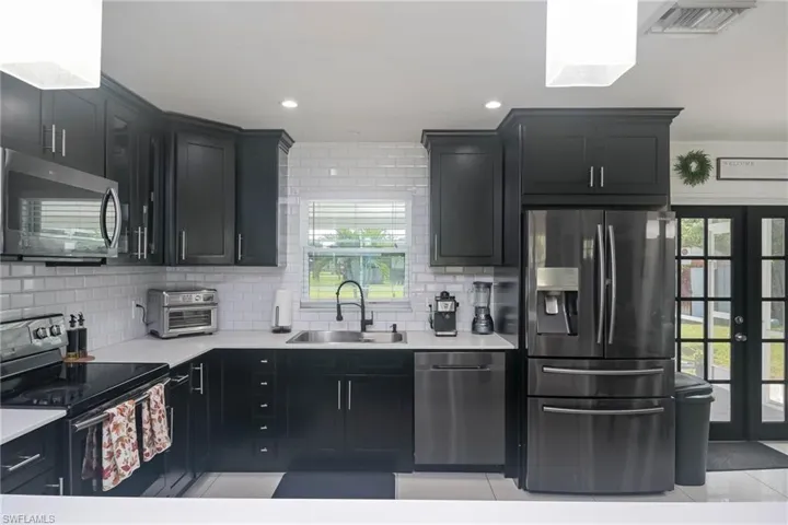 Kitchen with decorative backsplash, light tile patterned floors, sink, french doors, and stainless steel appliances