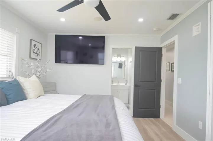 Bedroom featuring ensuite bath, sink, crown molding, light wood-type flooring, and ceiling fan