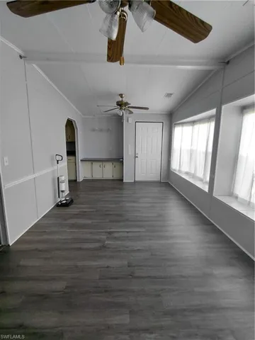 Unfurnished living room featuring arched walkways, dark wood finished floors, and ceiling fan