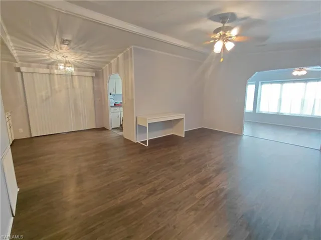 Unfurnished living room featuring dark wood finished floors, ceiling fan, a chandelier, crown molding, and arched walkways